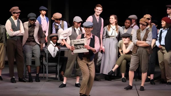 Un grupo de estudiantes está en el escenario de la Sidwell Friends School sosteniendo accesorios y documentos.