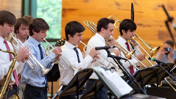 Un grupo de jóvenes músicos de la Sidwell Friends School toca instrumentos de metal en un escenario frente a un fondo de madera.