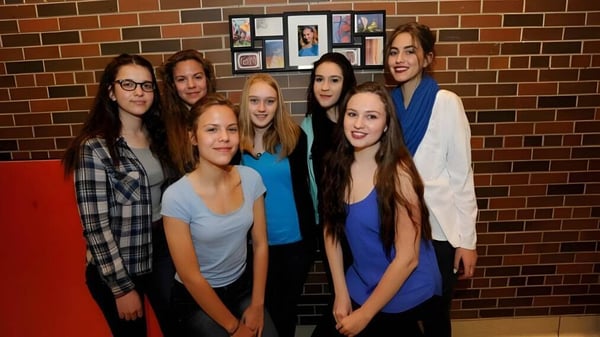 Un grupo de estudiantes está frente a una pared de ladrillo con fotos enmarcadas en el campus del Silverthorn Collegiate Institute.