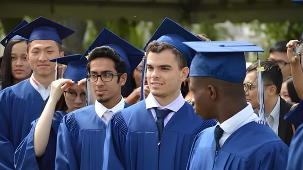 Un grupo de graduados está en togas y birretes azules frente a árboles en el campus del Silverthorn Collegiate Institute.
