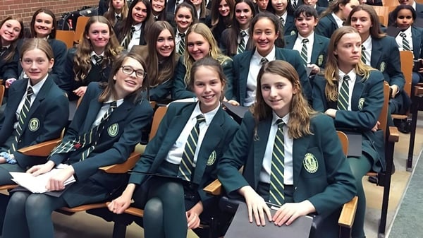 Un grupo de estudiantes en uniforme escolar está sentado en filas y sonríe a la cámara en el campus del Sir John A. Macdonald Collegiate Institute.