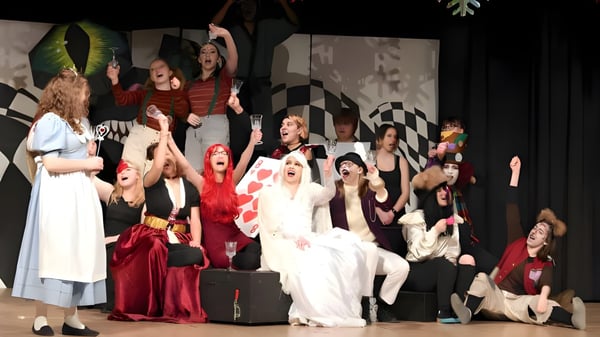 Estudiantes de la Sir Wilfred Laurier Secondary School actúan en coloridos disfraces en un escenario con fondo a cuadros.