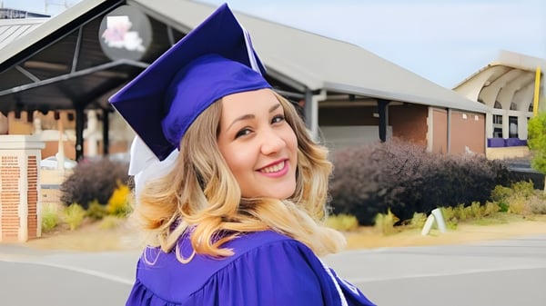 Una joven sonriente en vestimenta de graduación morada está frente a un edificio en el campus de la Sir Wilfrid Laurier Secondary School.