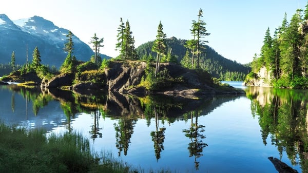 Un tranquilo lago alpino con montañas y bosques de coníferas se refleja en el terreno de la Sir Winston Churchill Secondary School.