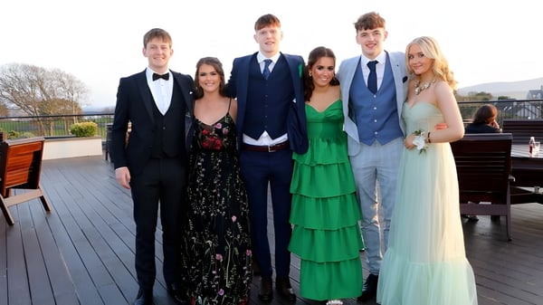 Un grupo de personas vestidas formalmente posan en una terraza de madera con un fondo paisajístico en el terreno de la Sligo Grammar School.