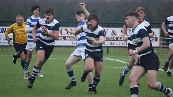 Estudiantes de la Sligo Grammar School juegan un intenso partido de rugby en un campo de hierba con un marcador en el fondo.