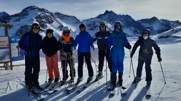Un grupo de estudiantes de la Sligo Grammar School está de pie con ropa de invierno en una pendiente cubierta de nieve con montañas al fondo.
