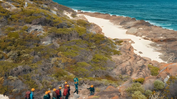 Un grupo de estudiantes camina por un sendero costero con vistas a un océano turquesa y una playa de arena cerca de la Smithfield State High School.