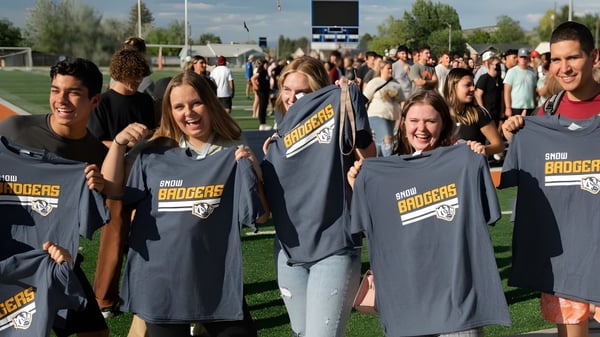 Un grupo de estudiantes con camisetas de Snow College se reúne en el campo deportivo frente a los espectadores.