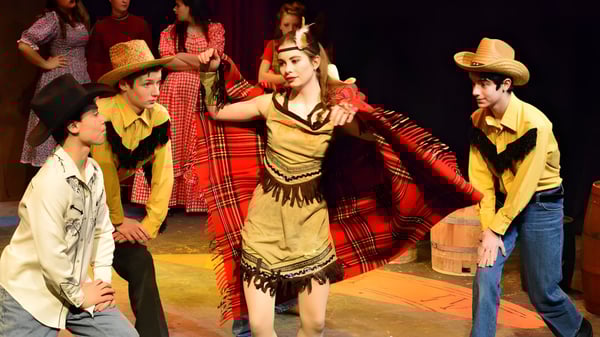Estudiantes de la Solebury School realizan una danza cultural tradicional en un escenario con un fondo oscuro.
