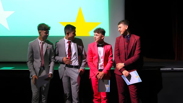 Cuatro personas vestidas formalmente están de pie frente a un telón de fondo con una gran estrella amarilla en el campus de la Somerset Studio School.