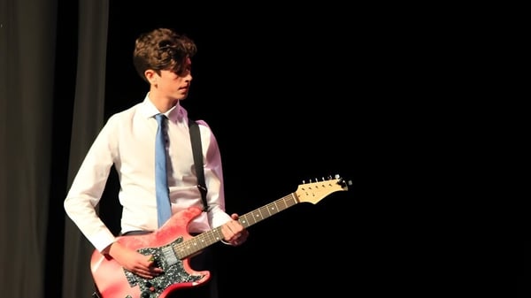 Una persona toca una guitarra eléctrica en un escenario oscuro en la Somerset Studio School.