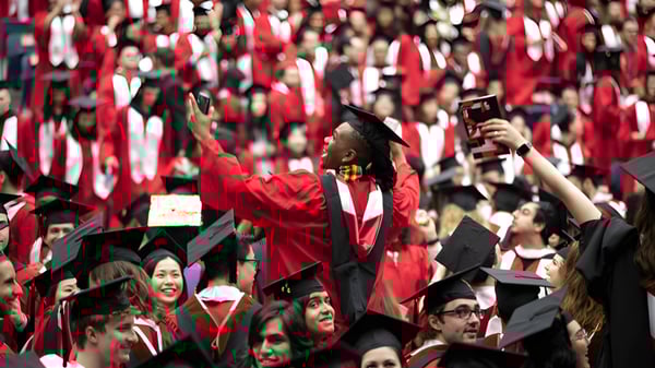 Un gran grupo de graduados en togas rojas celebra en la fiesta de graduación de la Somervale School en un salón interior.