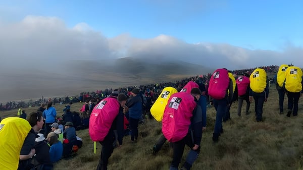 Estudiantes de la Somervale School están de pie en una ladera cubierta de hierba con ropa de lluvia colorida frente a montañas neblinosas.