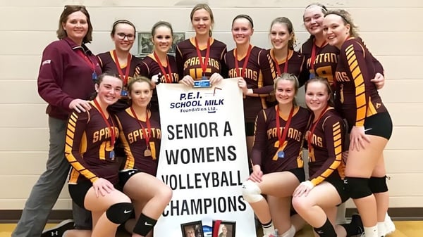 Estudiantes de la Souris Regional School celebran como campeonas de voleibol Senior A con un banner.