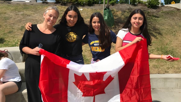 Cuatro estudiantes de la South Delta Secondary School sostienen juntas una gran bandera canadiense al aire libre.