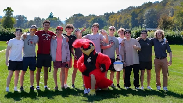 Un grupo de estudiantes está en el campo de deportes de la South Kent School frente a un fondo boscoso.