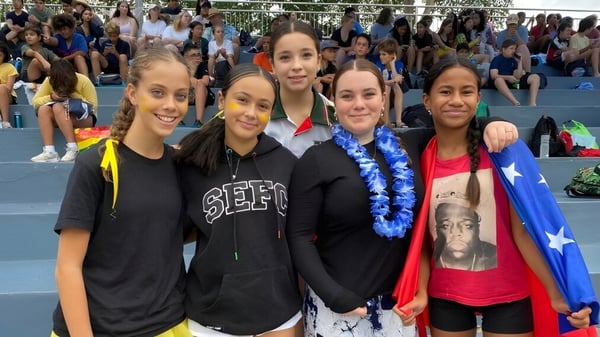 Un grupo de jóvenes estudiantes posa junto en el campus de la South Sydney High School con una multitud más grande al fondo.