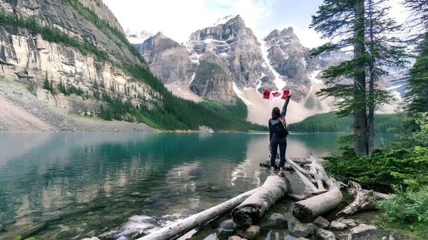 Una persona está de pie sobre un tronco caído frente a un lago con montañas nevadas al fondo en la South Carleton High School.