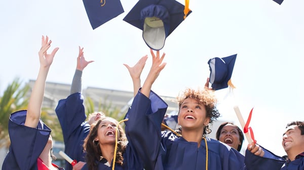 Un grupo de graduados de la Southport State High School lanza sus birretes azules al aire en una celebración al aire libre.