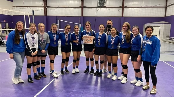 Un grupo de jóvenes jugadoras de voleibol de la Southwest Christian Academy sostiene juntas un trofeo en el gimnasio.