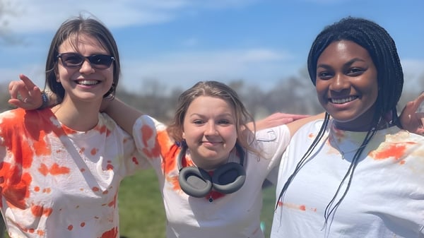 Tres estudiantes de la Sparhawk School posan sonrientes al aire libre en un prado verde bajo un cielo azul.