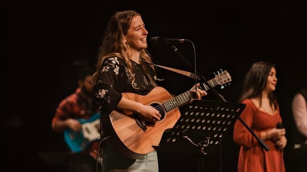Una estudiante de la Spectrum Community Secondary School toca la guitarra acústica en un escenario con otros músicos.