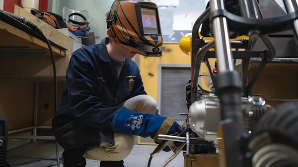 Una persona lleva una máscara de soldador y ropa de protección y trabaja en una máquina en el taller del Spotswood College.