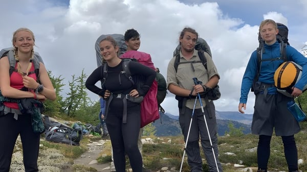 Un grupo de alumnas de la Spring Street International School está en equipo de senderismo en un paisaje montañoso con nubes y cielo azul.