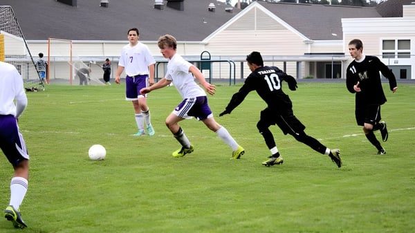 Estudiantes de la Spring Street International School juegan un partido de fútbol en el campo deportivo frente a un edificio escolar.