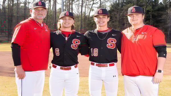 Cuatro estudiantes de la Springwood School llevan uniformes de béisbol y están juntos en el bosque.