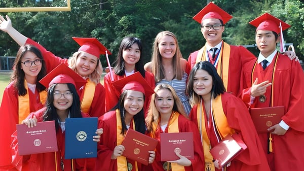 Un grupo de graduados de la Springwood School posan al aire libre con togas rojas y diplomas.