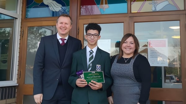Una estudiante de St. Alban's Catholic High School recibe un premio de adultos frente al edificio con coloridos vitrales.