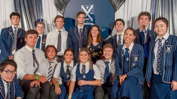 Un grupo de estudiantes del St. Andrew's College está junto a un banner con el logo de la escuela.