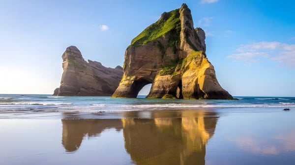 Vista de formaciones rocosas con tonos verdes y amarillos sobre agua tranquila en el terreno del St. Andrew's College.