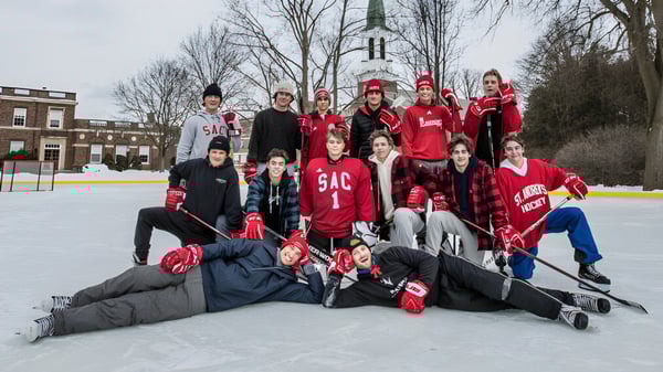 Un grupo de estudiantes del St. Andrew’s College se reúne en una pista de hielo con un fondo de campanario.