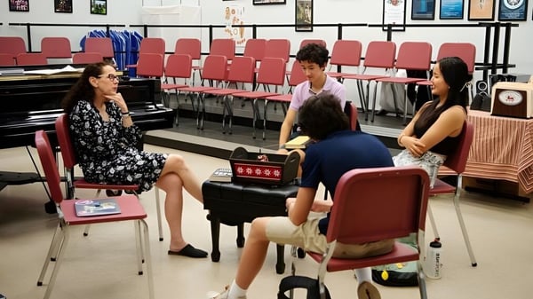 Un grupo de estudiantes está sentado en el aula de la St. Andrew's School con sillas y un piano al fondo.