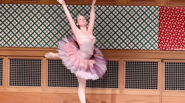Una bailarina en tutú rosa y leotardo realiza una elegante pose de danza frente a un patrón colorido en la St. Andrew's School.