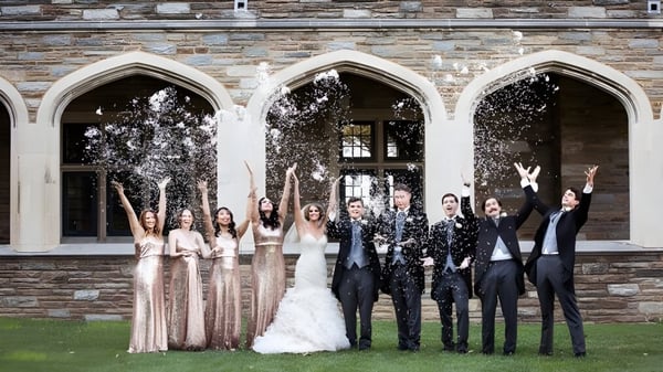 Estudiantes de la St. Andrew's School celebran frente a un edificio histórico con ventanas de arco y lanzan confeti al aire.