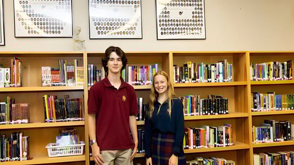 Dos alumnas y alumnos están frente a una estantería en la biblioteca de la St. Anne's Catholic School.