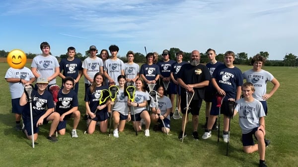 Un grupo de alumnas y alumnos de la St. Anne's Catholic School posan juntos en un campo deportivo bajo un cielo azul.