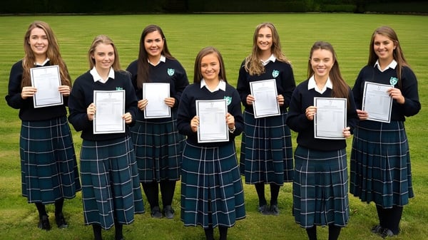 Seis estudiantes de St. Anne's Secondary School están al aire libre sosteniendo sus certificados en un entorno verde.