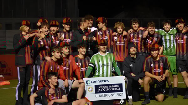 Un grupo de jóvenes futbolistas con camisetas rojas y negras celebra la victoria del campeonato en el campo de St. Bede's College.