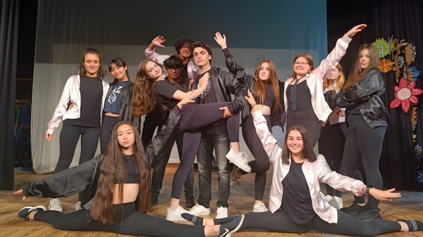 Un grupo de estudiantes de la St. Bees School posan juntos en un escenario con fondo oscuro.