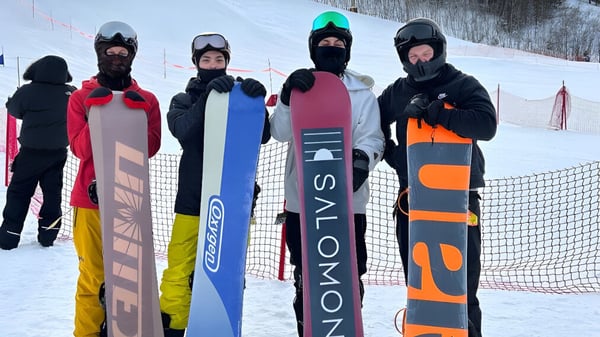 Un grupo de estudiantes de la St. Benedict Catholic Secondary School lleva ropa de esquí colorida y está frente a una pista cubierta de nieve.
