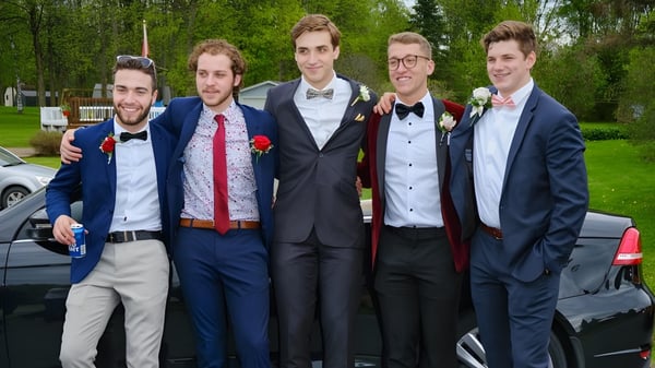 Un grupo de estudiantes del St. Benildus College está vestido formalmente al aire libre en un prado con árboles de fondo.
