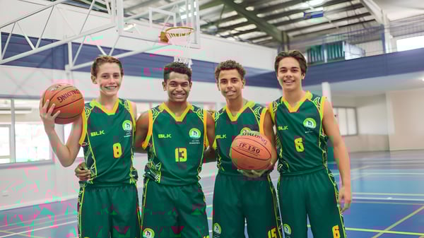 Cuatro estudiantes del St. Brendan's College están en la cancha de baloncesto juntos con camisetas verdes.