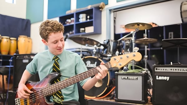 Un estudiante del St. Brendan's College toca la guitarra eléctrica en un estudio de música con instrumentos musicales de fondo.