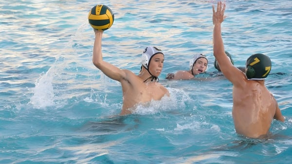 Dos estudiantes de la St. Brendan’s Community School juegan al voleibol en la piscina bajo un clima soleado.