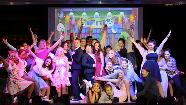 Un grupo de jóvenes mujeres realiza una actuación en el escenario de St. Brigid's College frente a coloridos telones.